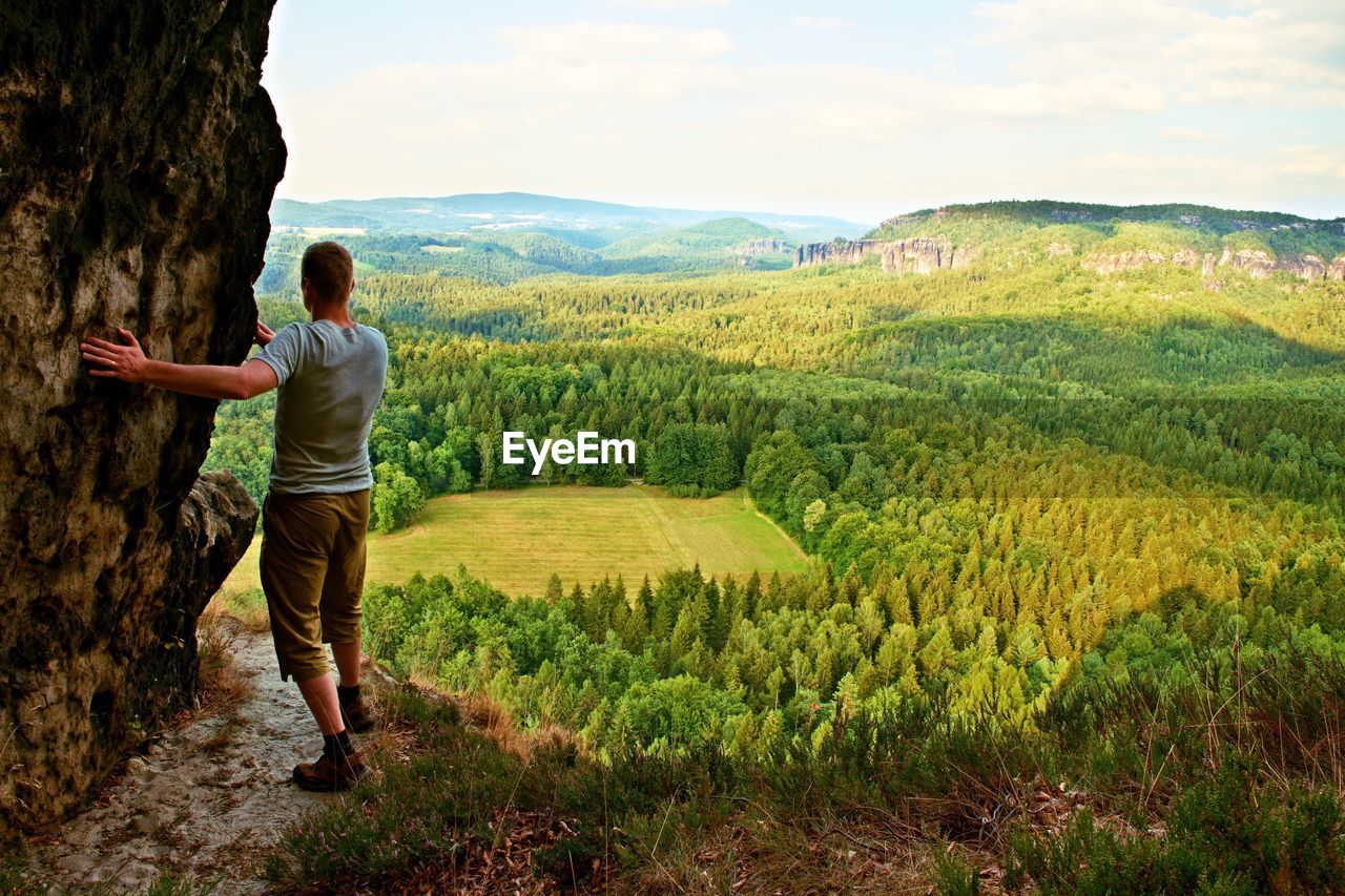 Tourist climbing on sharp cliff hold careful rock side  and overlooking view above forest valley
