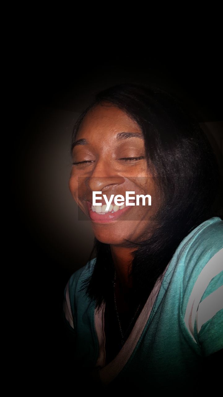 Close-up of smiling young woman against black background