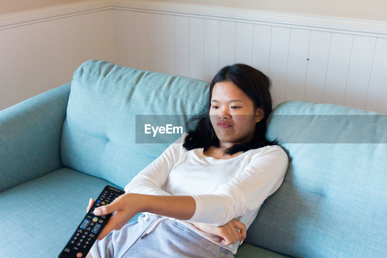 Asian teenage girl sitting on sofa watch television