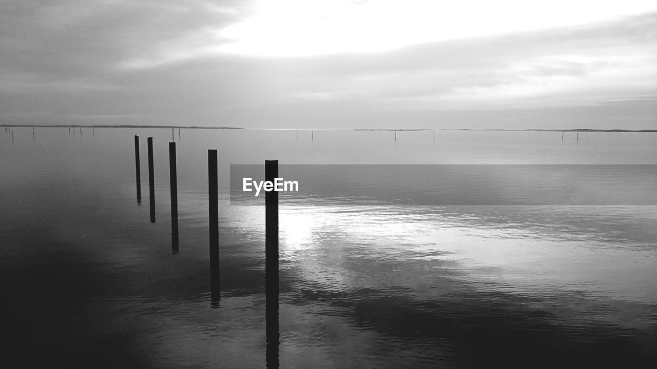 Wooden posts in sea against cloudy sky during sunset