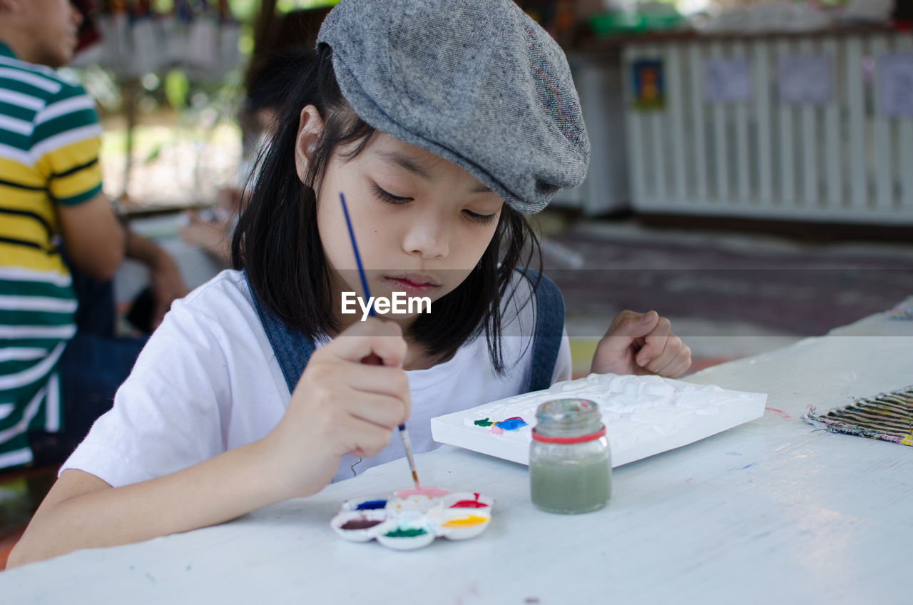 Close-up of girl with brush and watercolor paints sitting on table