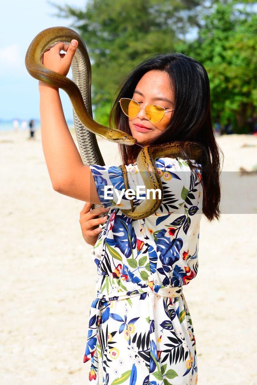 Young woman holding snake while standing at beach