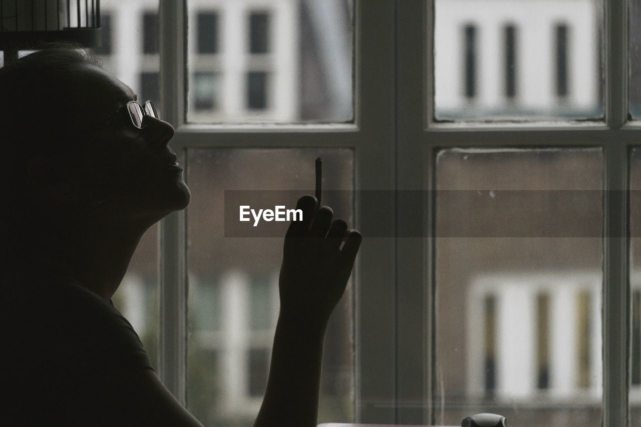 Side view of woman smoking cigarette against glass window