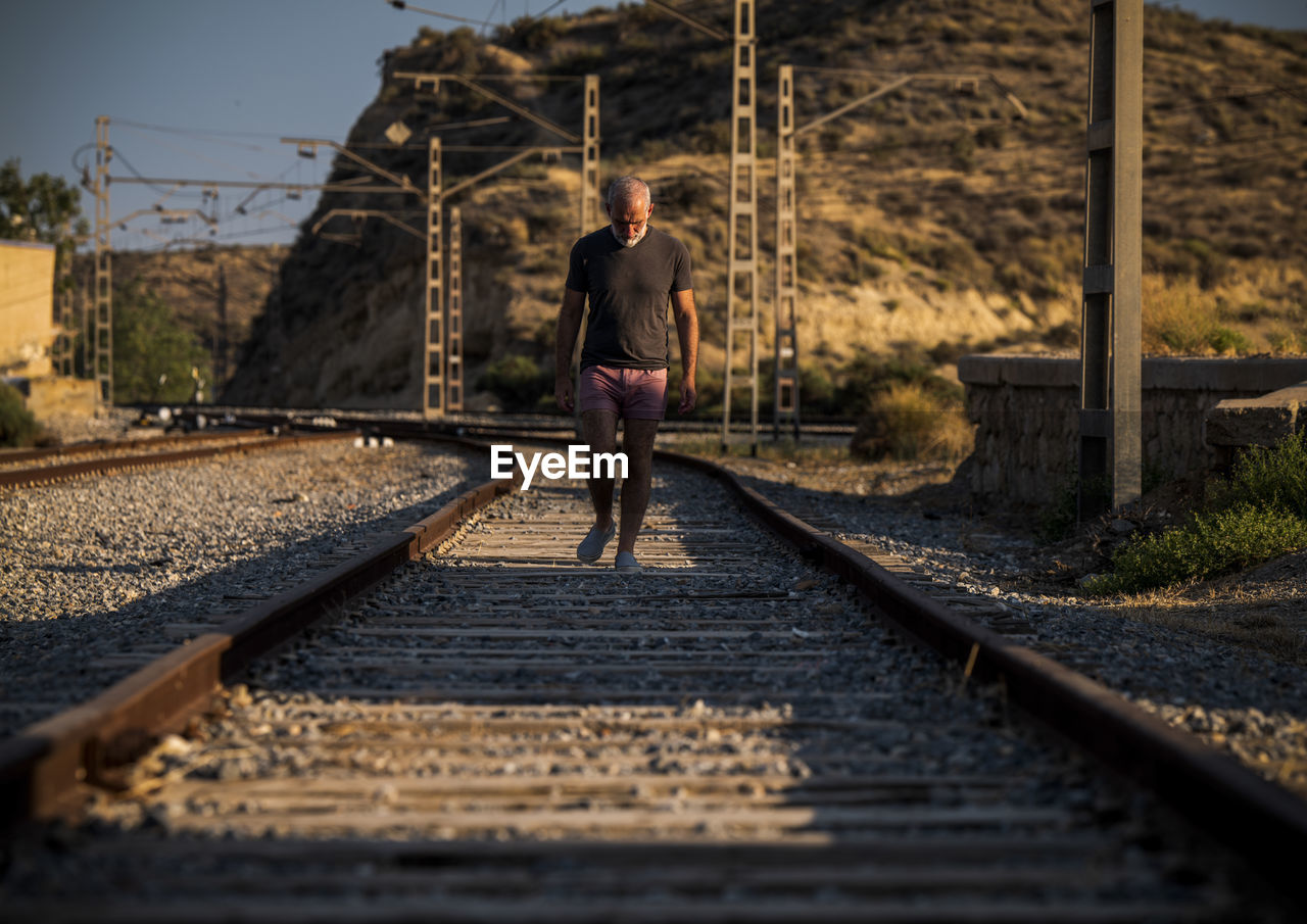 Man walking on railroad track in summer with sunlight and shadow