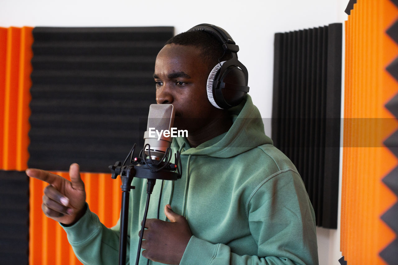 Young male rapper rapping on microphone while recording song in studio