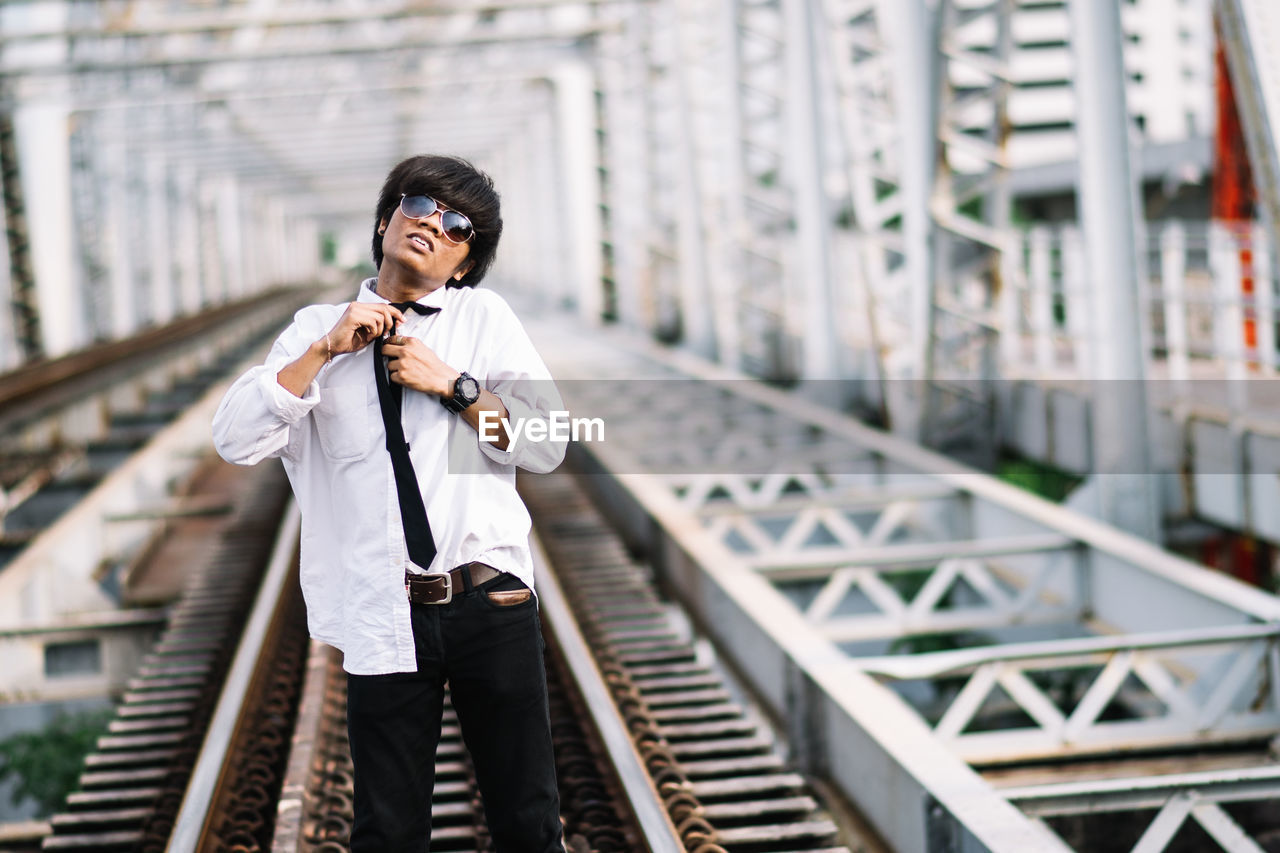 Portrait of young man getting dressed while standing on railroad track