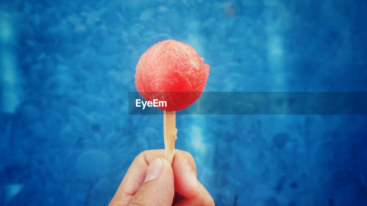 Cropped image of person holding watermelon lollipop