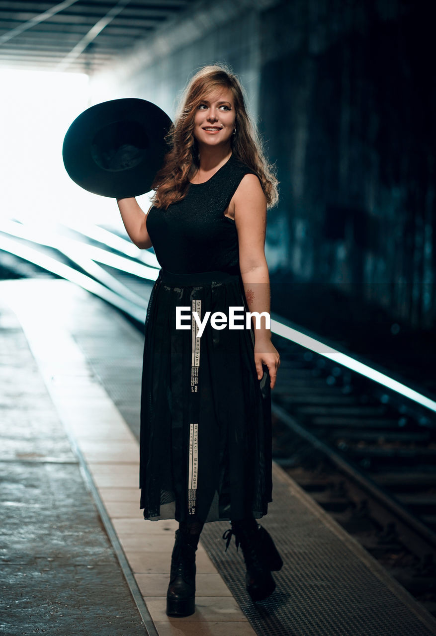 Full length of woman holding hat standing on railroad station platform