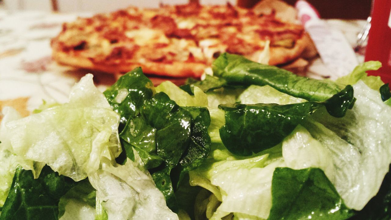 Close-up of salad with pizza in background