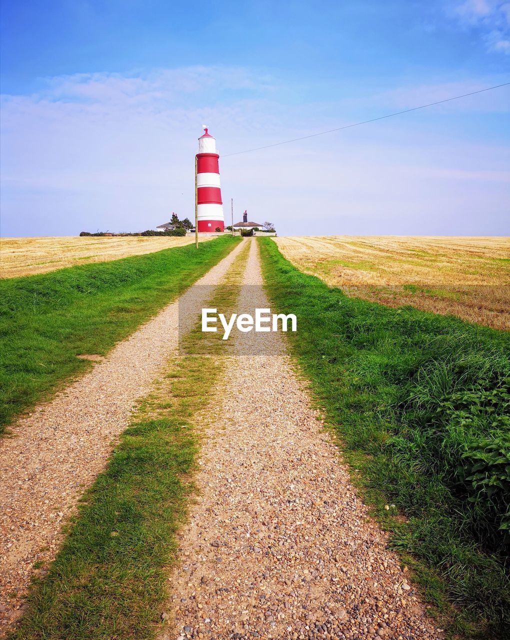 Road leading towards lighthouse amidst field against sky