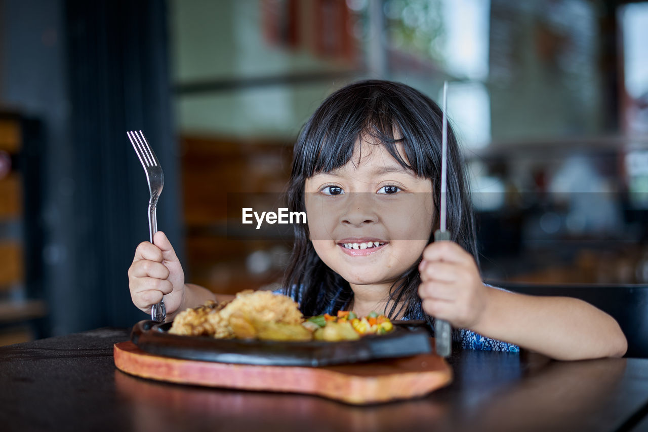 Close-up portrait of smiling girl with food on table in restaurant