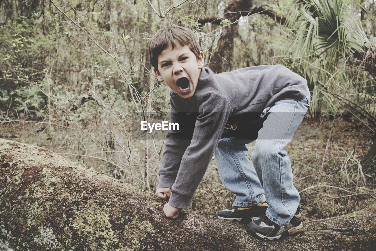 Full length side view of boy imitating gorilla in forest