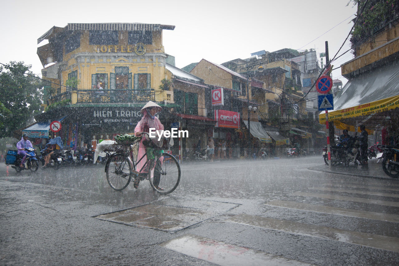 PEOPLE RIDING BICYCLE ON ROAD IN RAIN