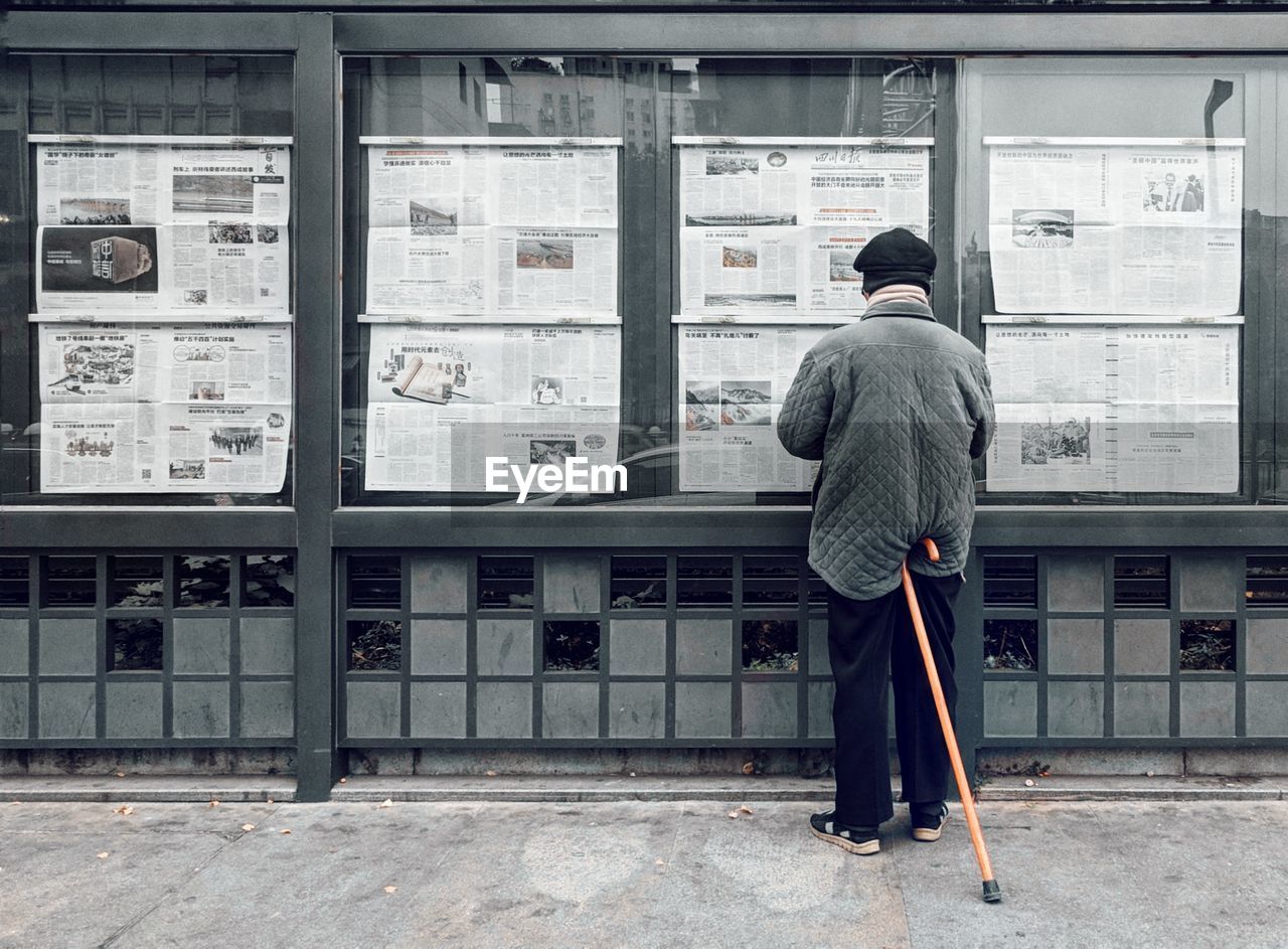 Rear view of mature man reading newspaper while standing on street