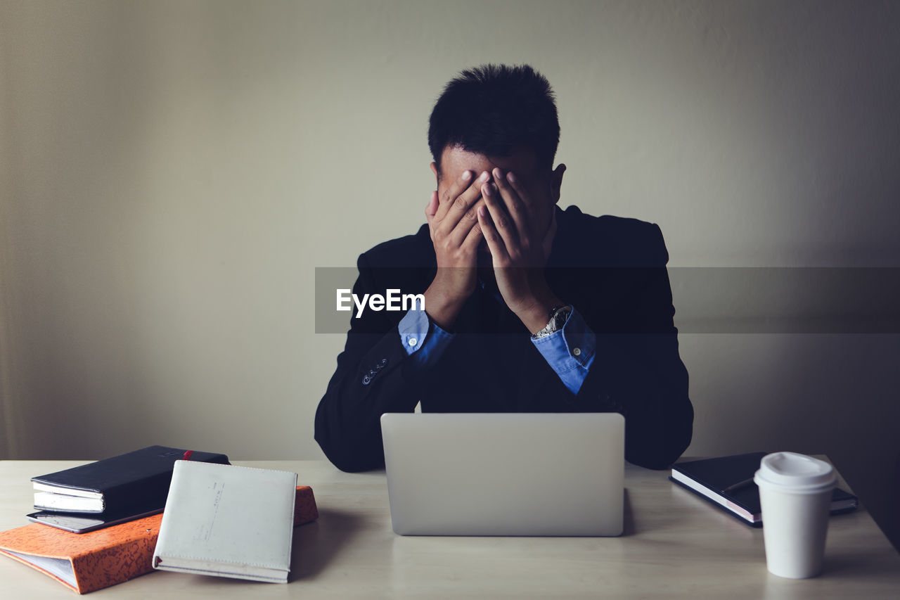 Frustrated businessman covering face while sitting on table