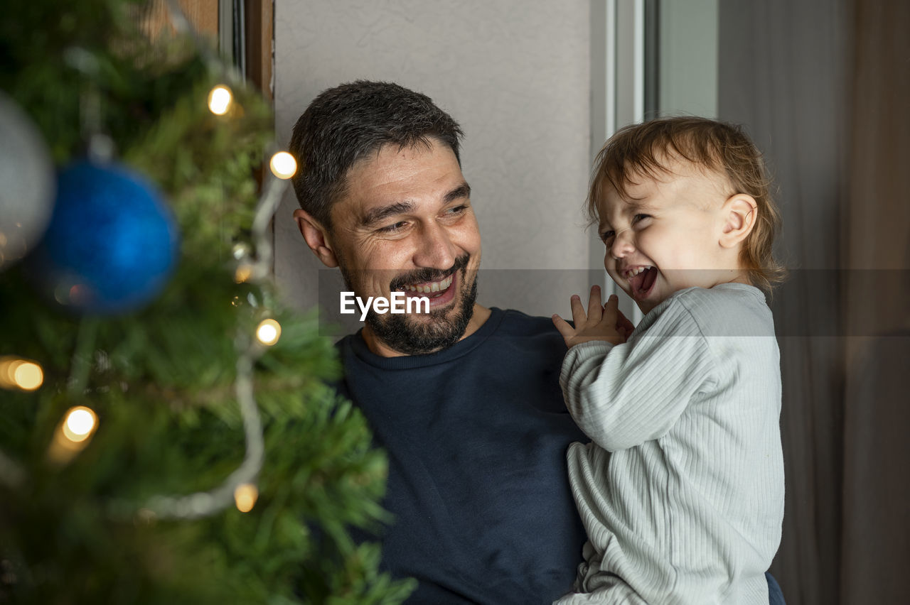 Happy father carrying cute boy in front of christmas tree at home