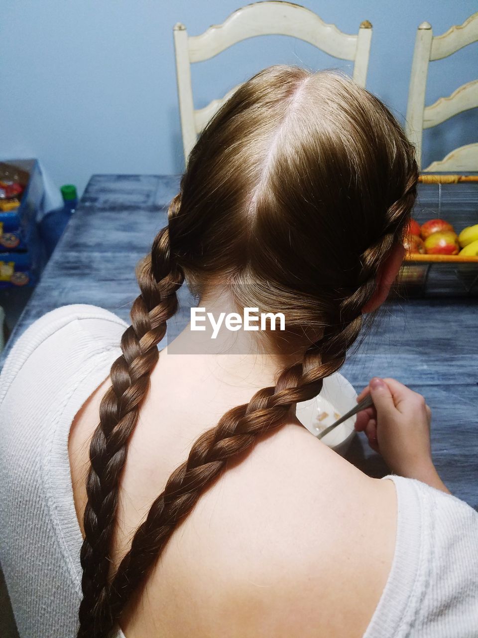Rear view of teenage girl with braided hair sitting by table at home