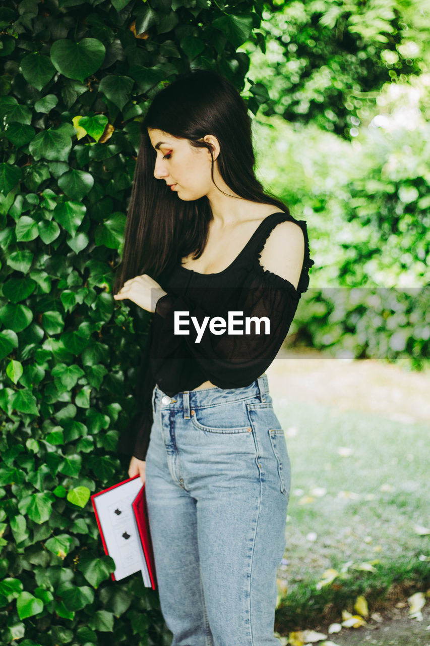 Side view of young woman standing against plants