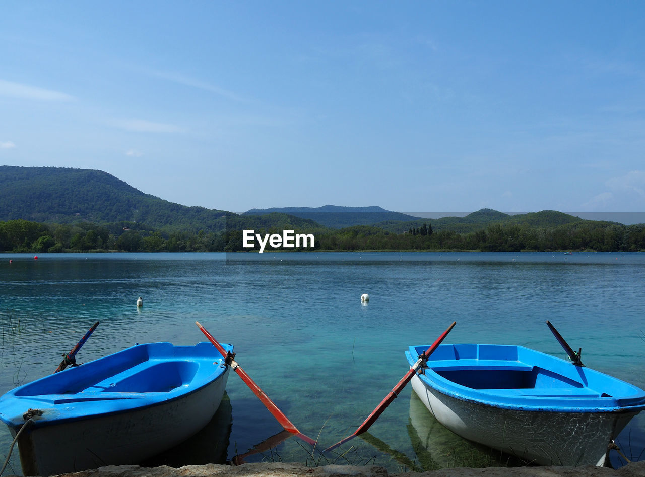 Boats moored on lake against blue sky