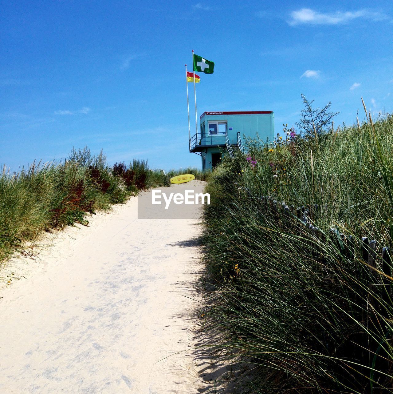 Flags on lifeguard hut by grass against sky at sandy beach
