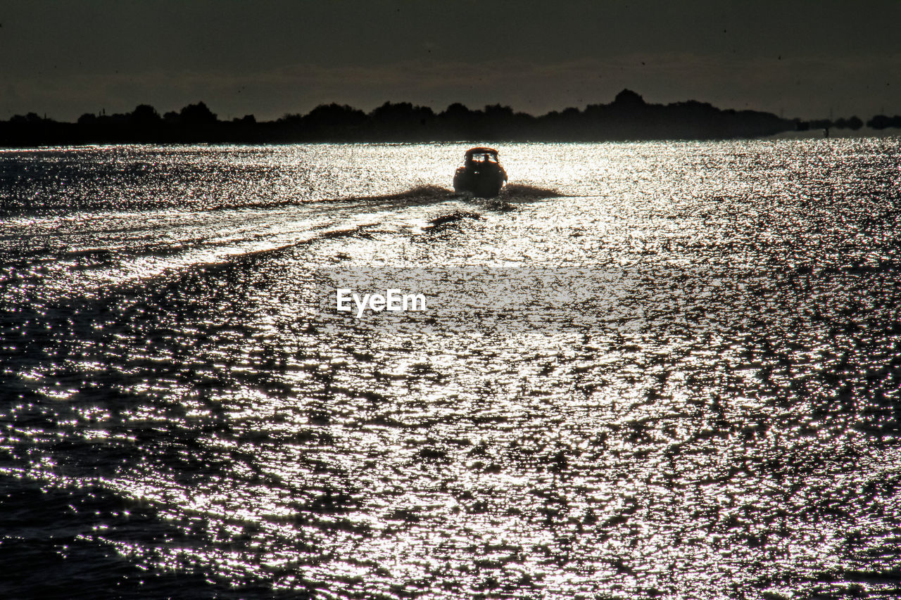 SILHOUETTE MAN IN BOAT ON LAKE AGAINST SKY