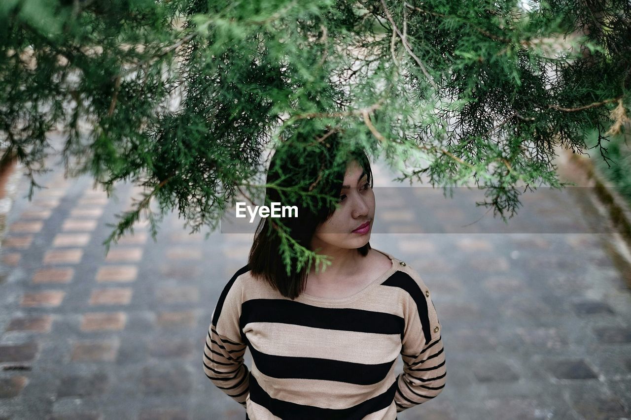YOUNG WOMAN STANDING AGAINST PLANTS