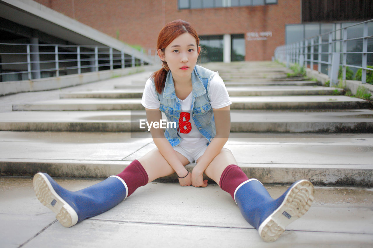 Full length portrait of young woman wearing rubber boots while sitting on steps