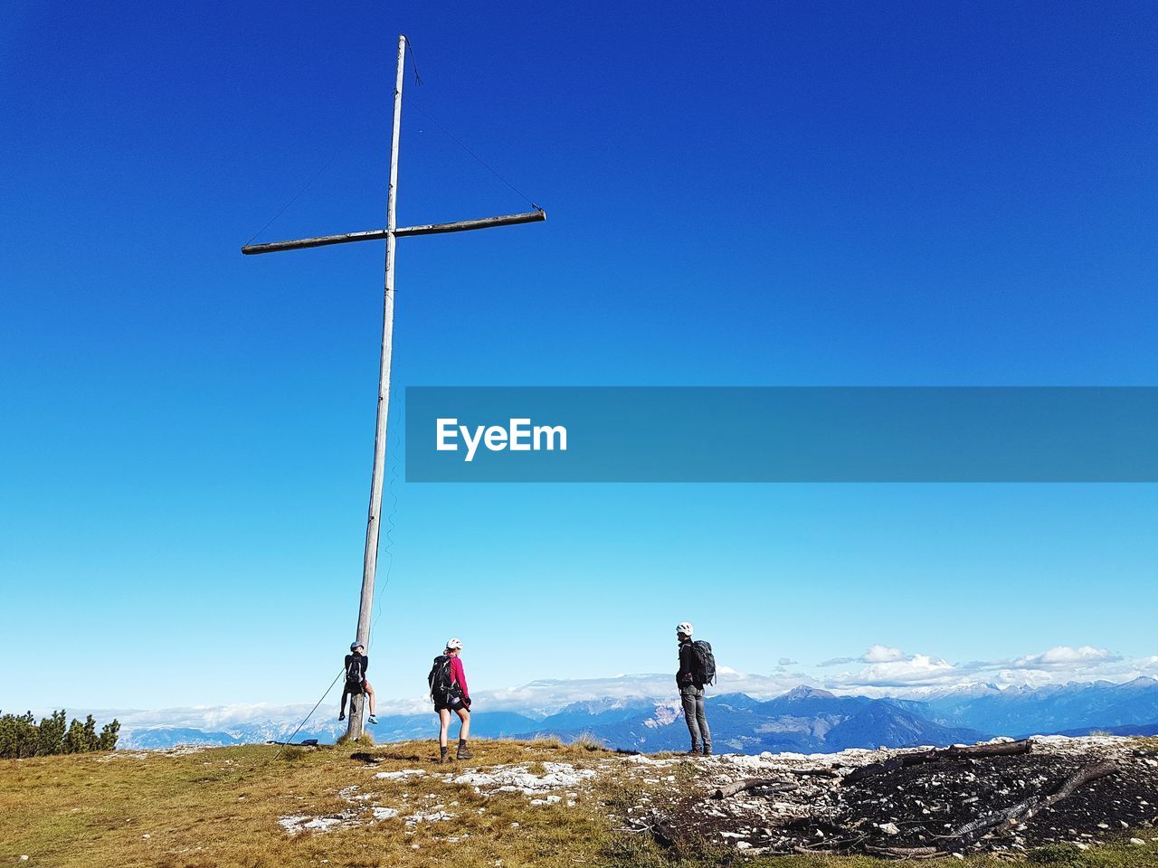 People standing by cross on mountain against clear blue sky