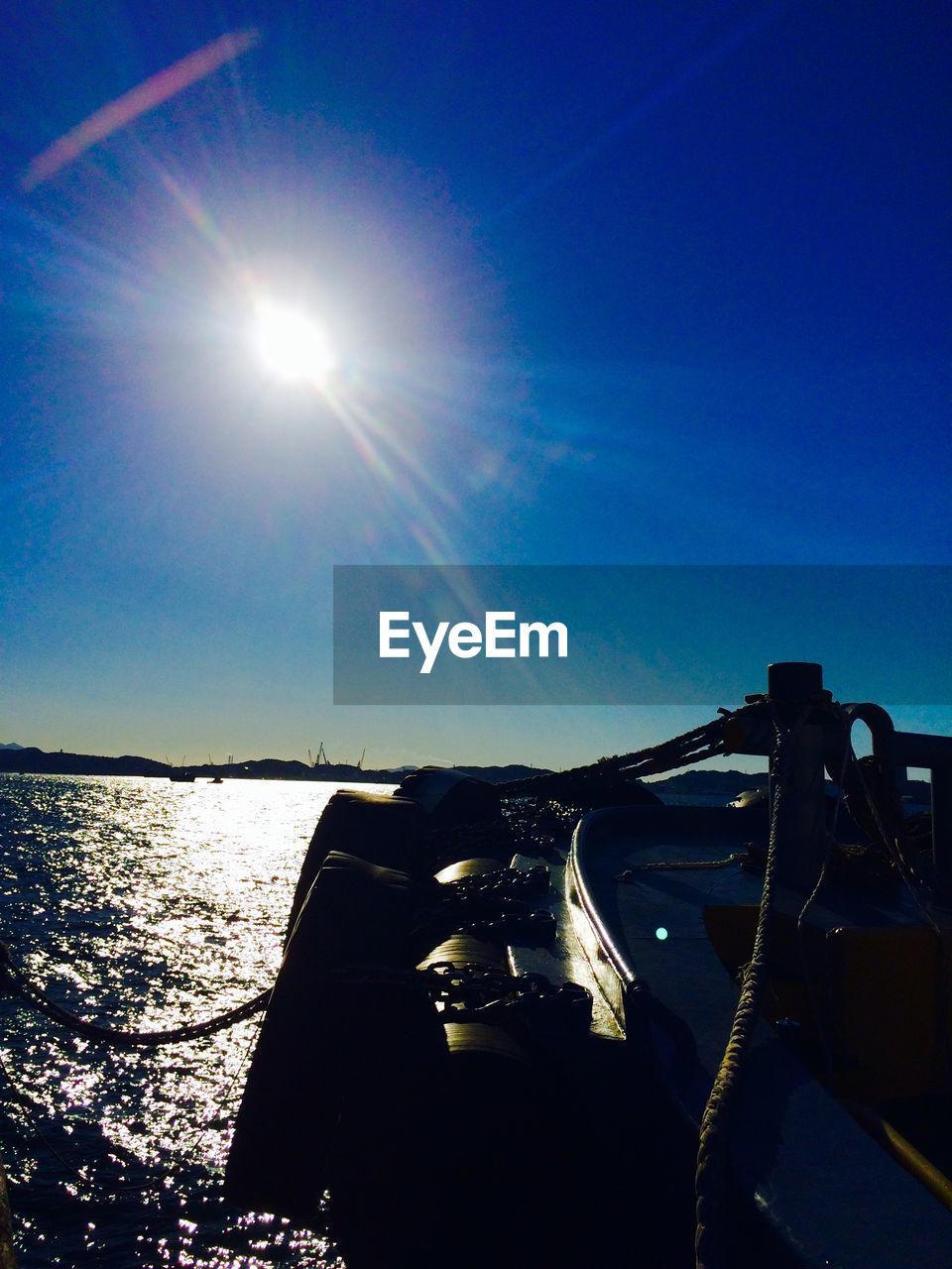 Boat moored on harbor against bright sun