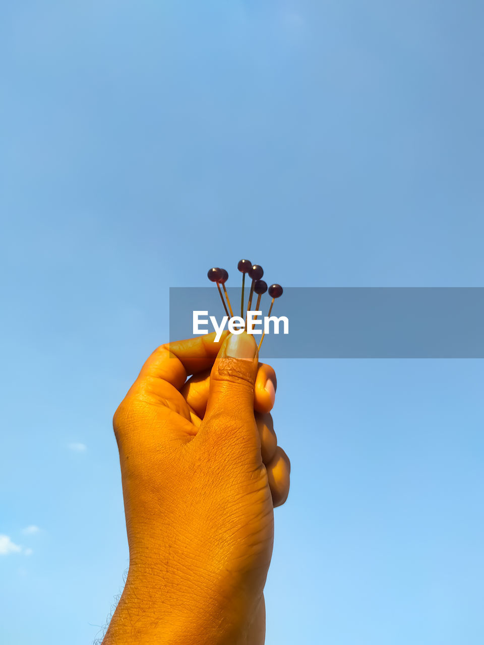 Cropped image of man holding needles against blue sky