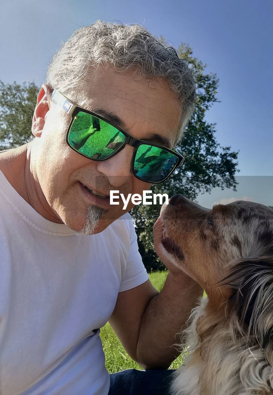 one animal, animal themes, animal, dog, mammal, pet, domestic animals, glasses, canine, adult, sunglasses, one person, men, senior adult, portrait, gray hair, smiling, mature adult, leisure activity, happiness, seniors, headshot, fashion, nature, emotion, friendship, day, lifestyles, carnivore, positive emotion, casual clothing, love, person, sky, eyeglasses, retirement, sunlight, outdoors, affectionate, bonding, human face, summer, enjoyment, cheerful, front view