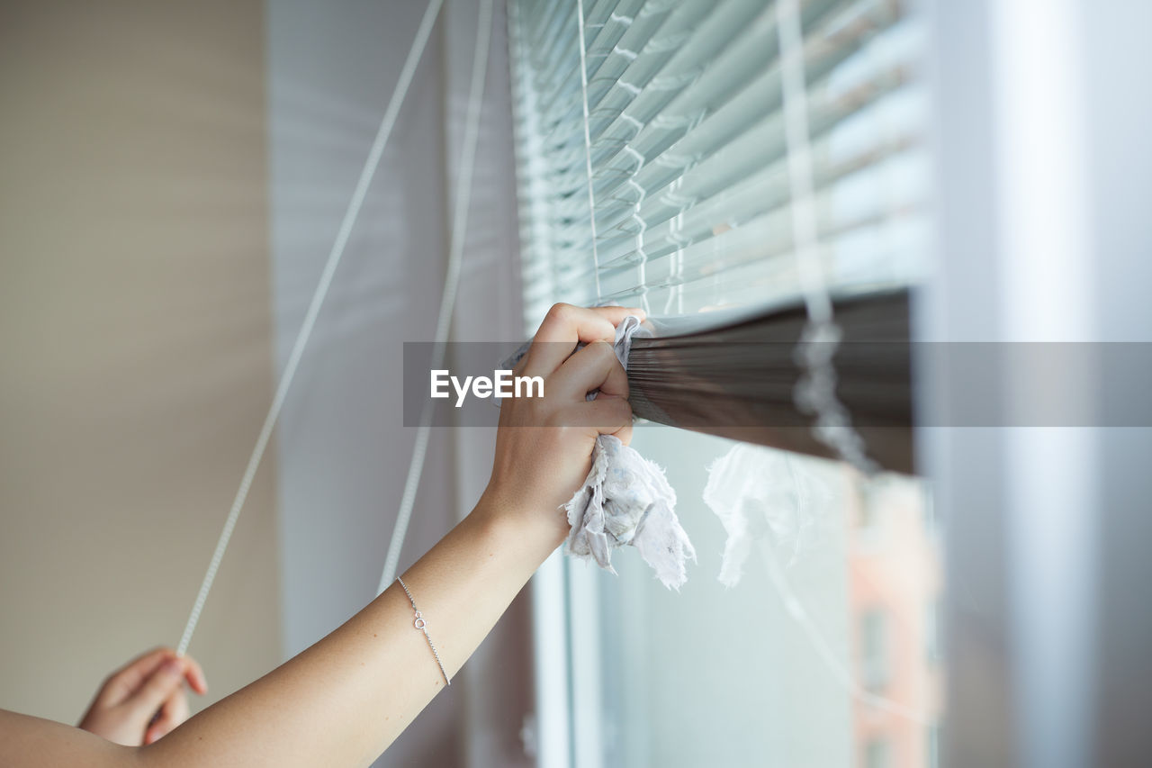 Midsection of person holding hands hanging on window