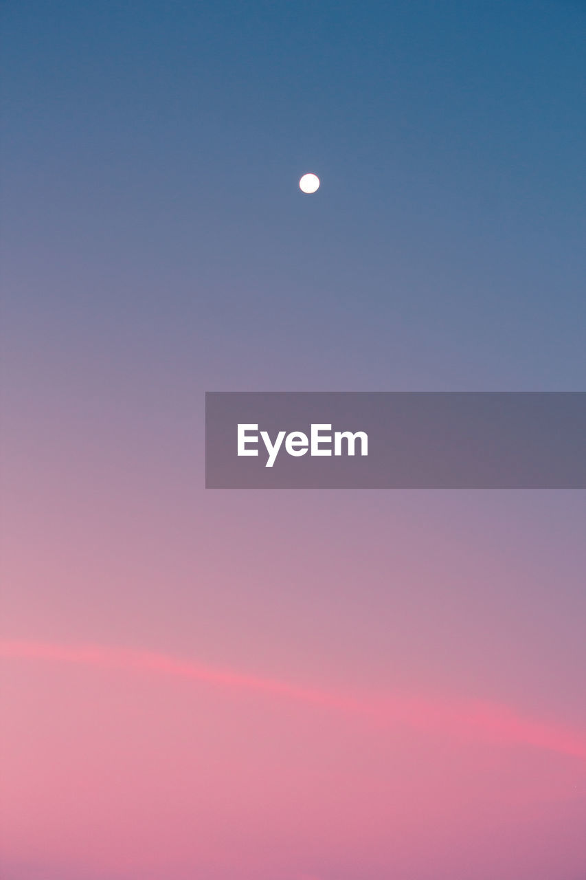 LOW ANGLE VIEW OF MOON AGAINST BLUE SKY AT SUNSET