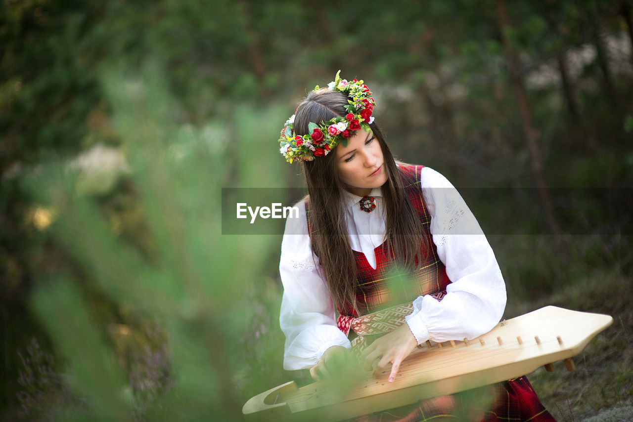 Woman playing koto while sitting against trees