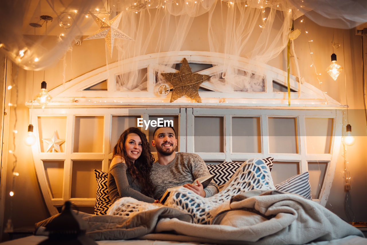 Young couple looking away while holding book on bed at home