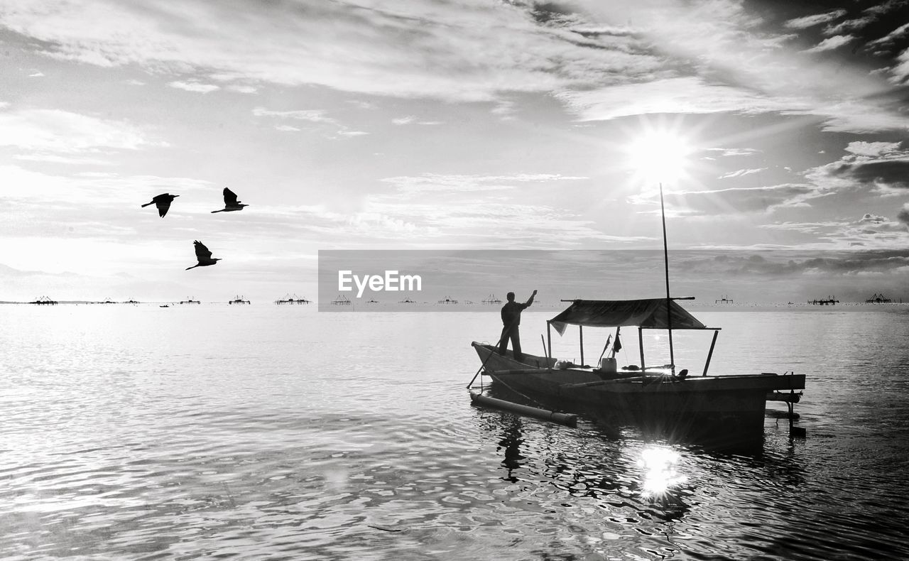water, sky, sea, nautical vessel, nature, transportation, black and white, cloud, monochrome photography, bird, mode of transportation, monochrome, beauty in nature, animal, animal themes, sunlight, scenics - nature, flying, day, wildlife, silhouette, tranquility, beach, vehicle, travel, ocean, outdoors, animal wildlife, horizon, shore, vacation, holiday, wave, trip, travel destinations, coast, tranquil scene, land, sun, ship, boat, men, reflection