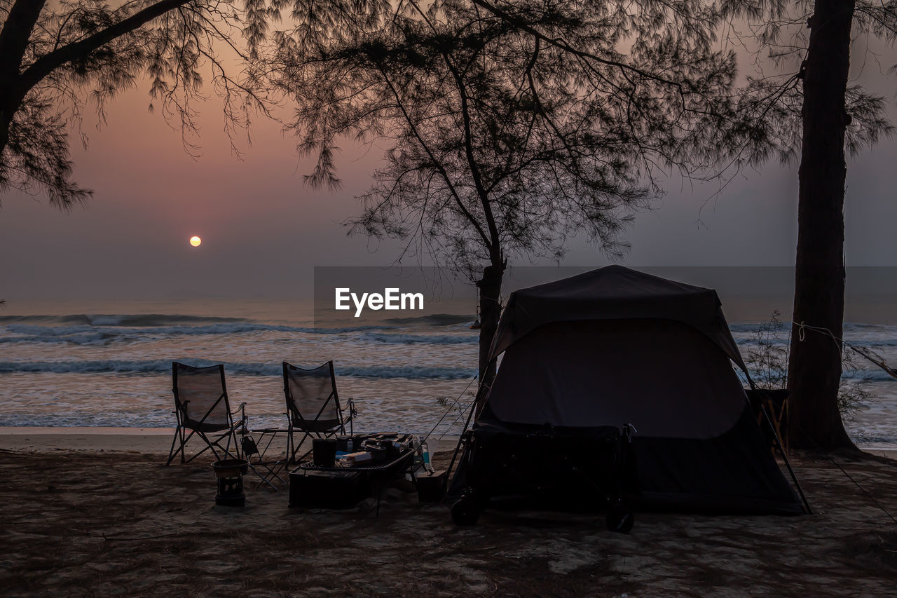 CHAIRS AND TABLES ON BEACH AGAINST SKY DURING SUNSET