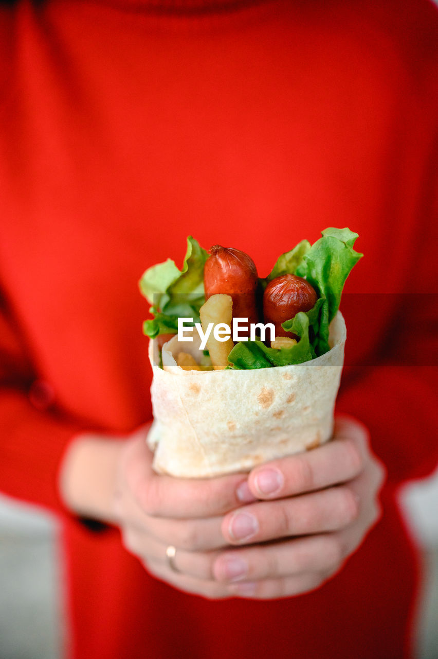 The hands of a girl in red clothes are holding fast street food. shawarma is food in pita