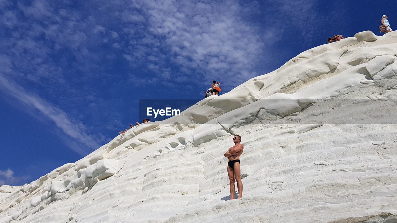 Low angle view of man climbing on mountain against sky