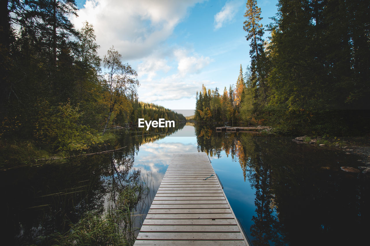 Wooden pier and still river reflect colourful autumn forest.  autumn in hossa national park, finland