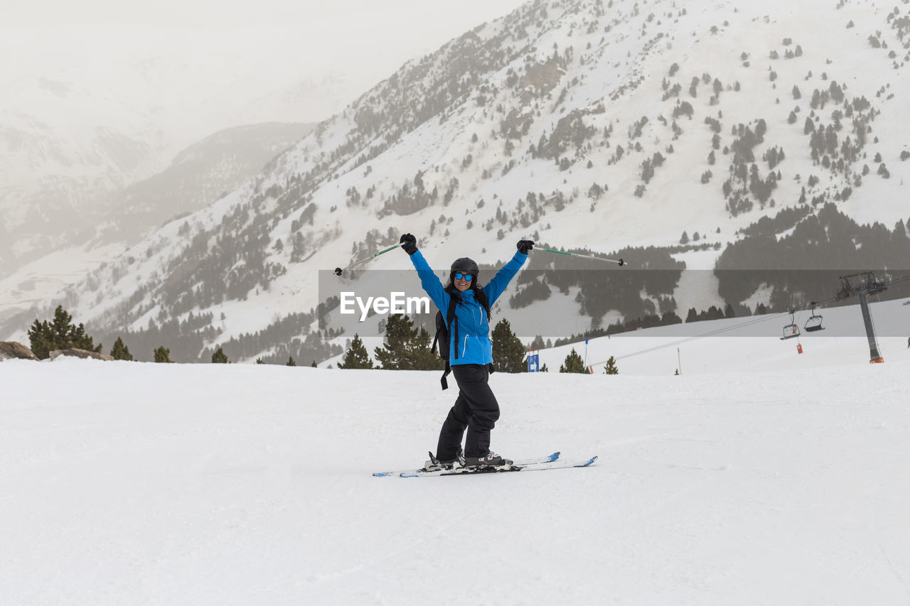 Portrait of smiling woman with arms raised skiing on snowcapped mountain