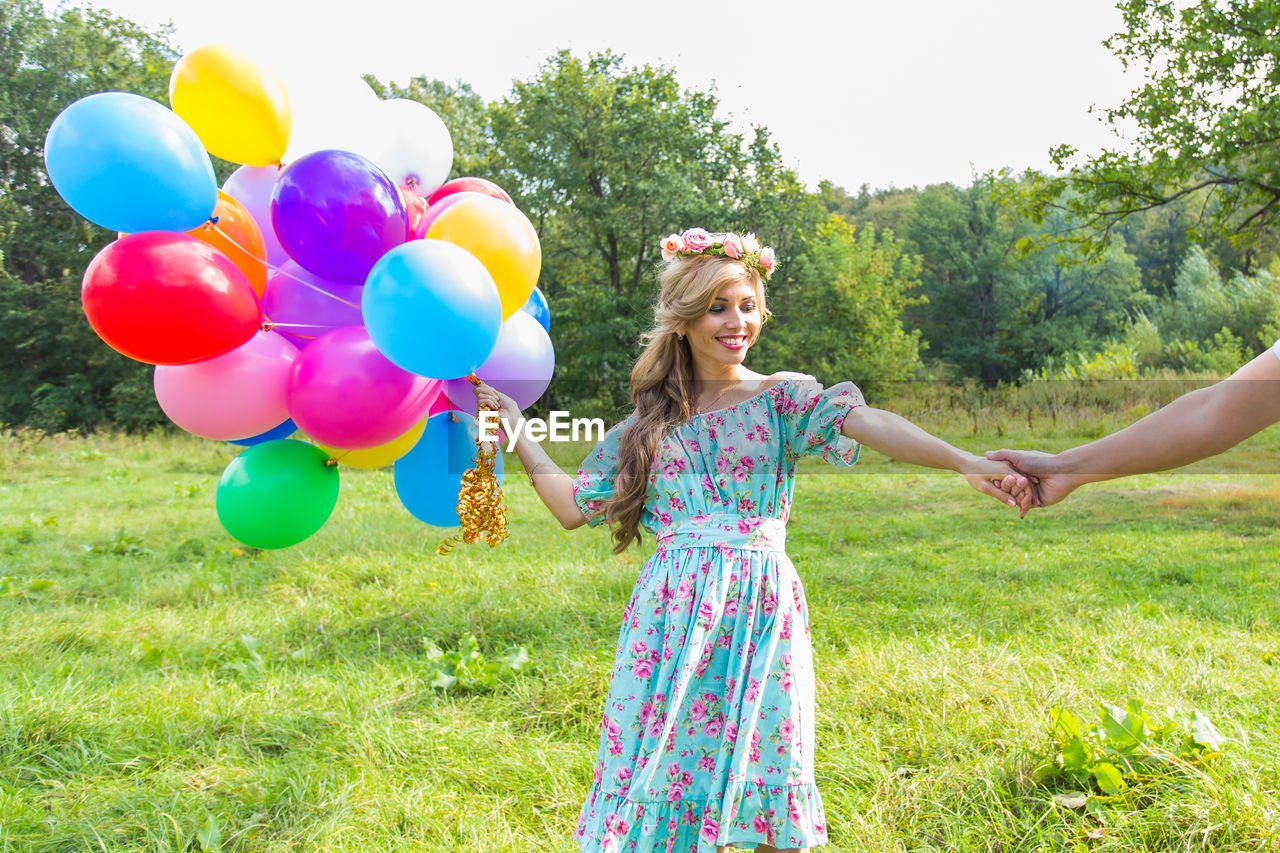 YOUNG WOMAN HOLDING BALLOONS IN FIELD
