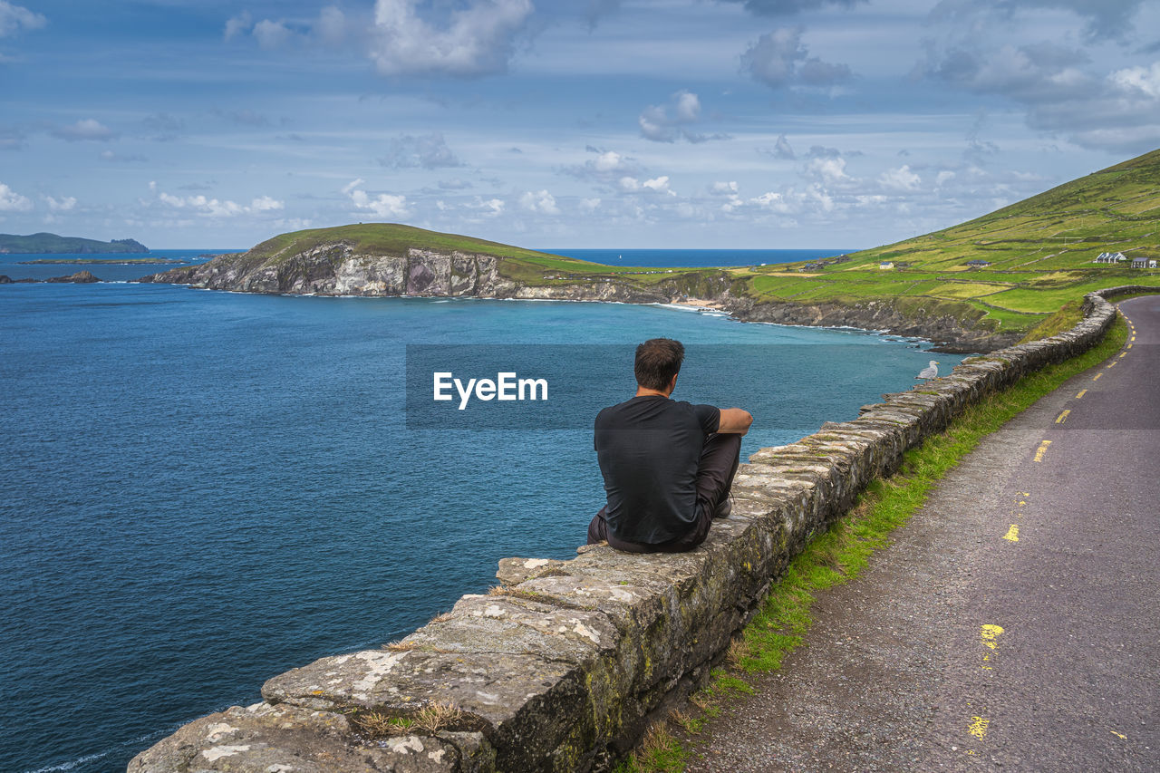 REAR VIEW OF PERSON LOOKING AT SEA AGAINST SKY