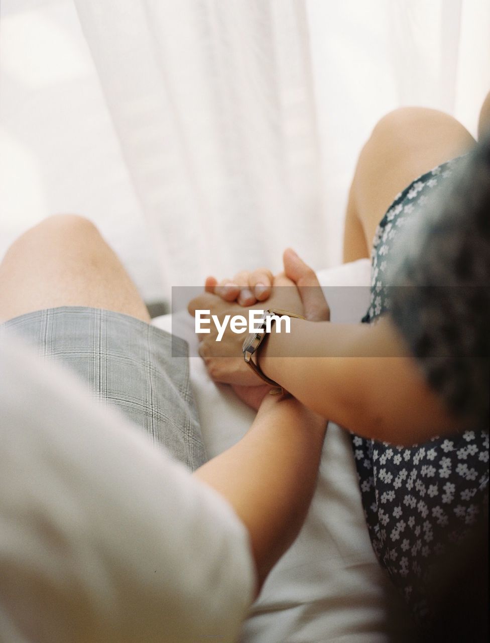 Midsection of couple holding hands while sitting on bed 