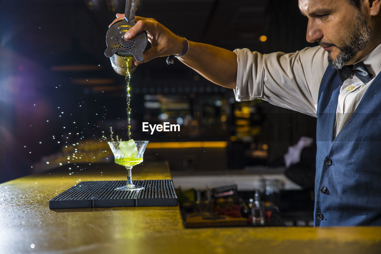 Side view of bartender pouring drink in glass on counter at bar