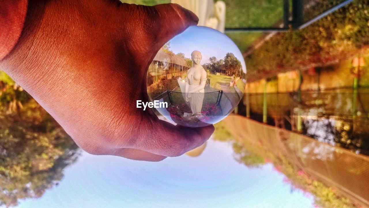 CLOSE-UP OF HAND HOLDING CRYSTAL BALL REFLECTION IN GLASS