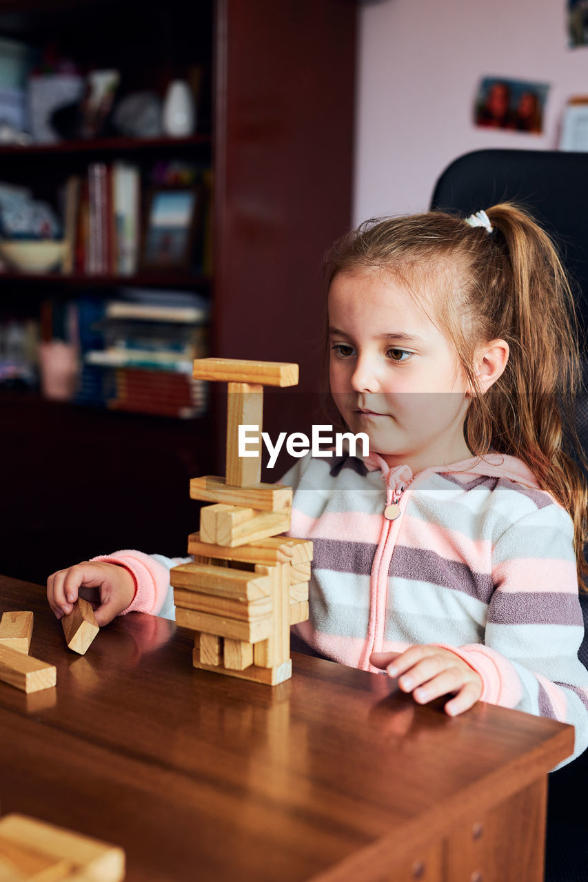 Cute girl playing with wooden blocks on table at home