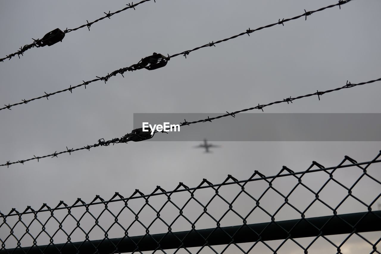 Close-up of barbed wire fence against sky