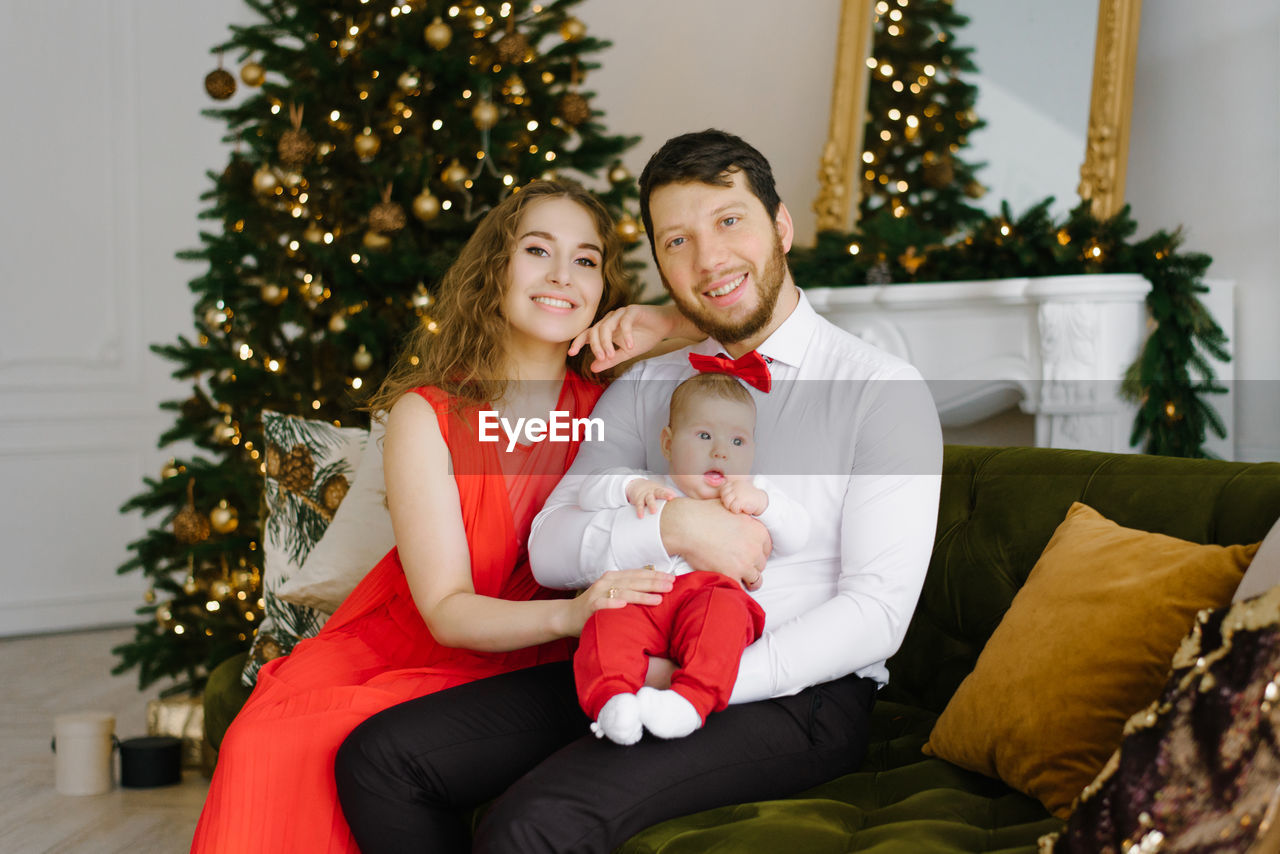 A young happy family with a child is sitting on a chair near a decorated christmas tree person