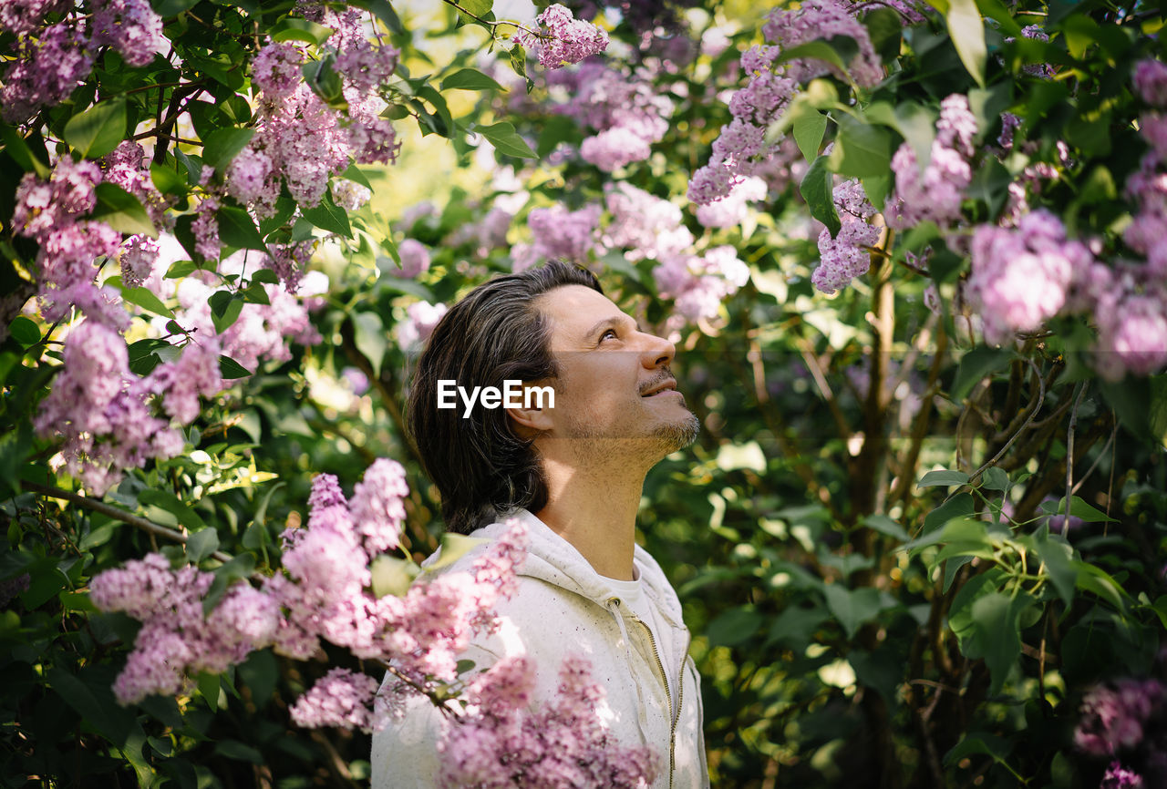 Portrait of smiling man standing by pink lilac flowers